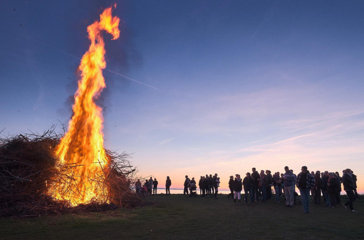 Bilden visar en stor brasa och en folksamling som står bredvid och beskådar elden som sträcker sig mot skyn.